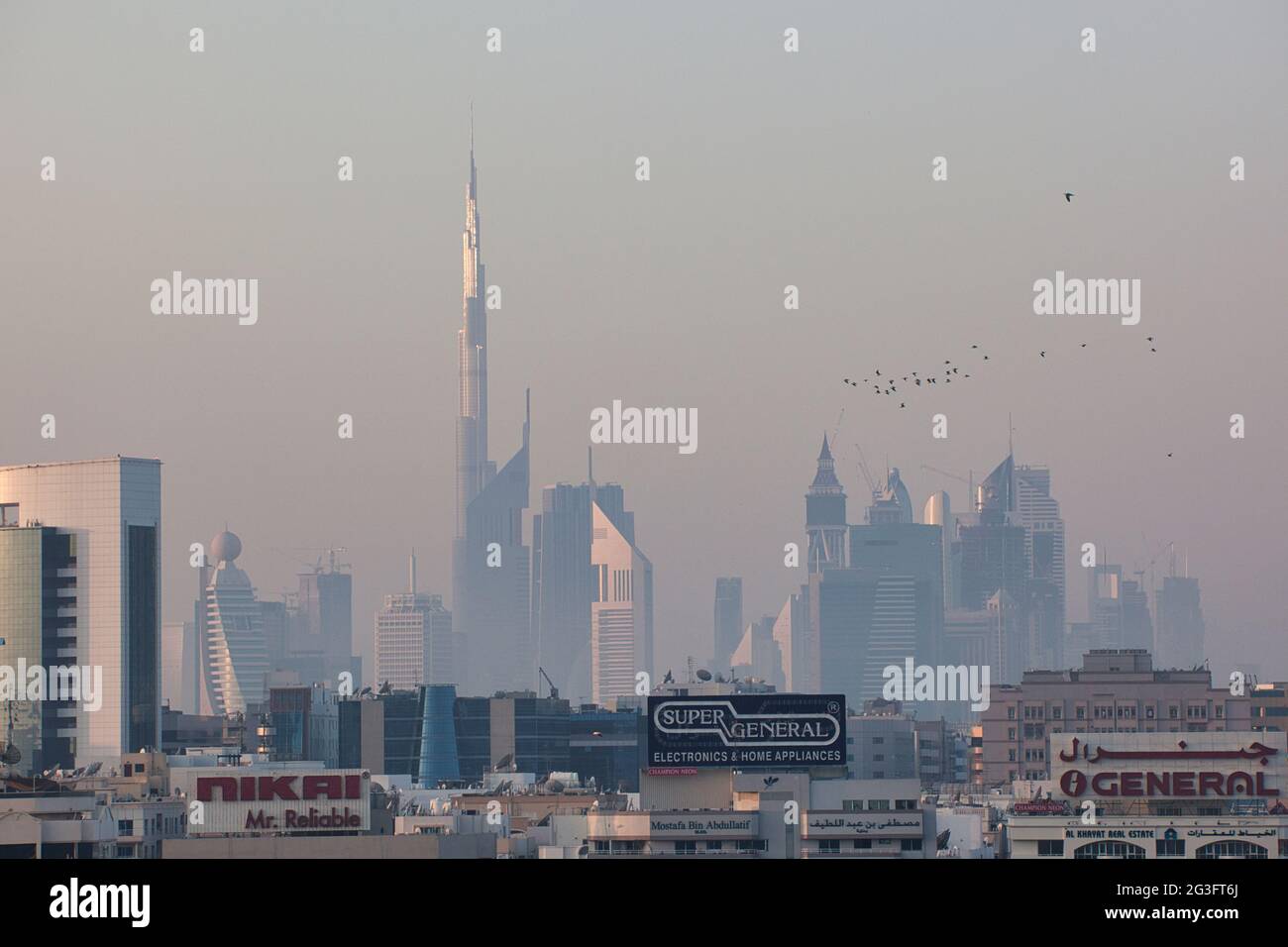 Lo skyline al tramonto del quartiere degli affari di Dubai, gli Emirati Arabi Uniti, con il Burj Khalifa, l'edificio centrale più alto del mondo e il gregge di uccelli nel cielo Foto Stock