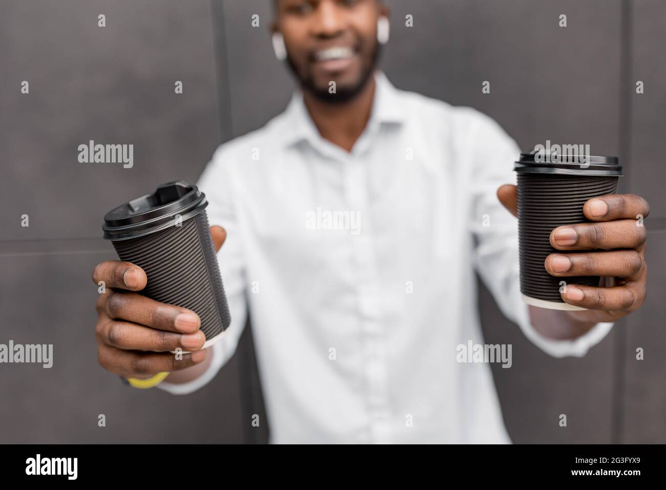 Bell'uomo sorridente afro americano in piedi all'aperto isolato e mostrando alla macchina fotografica due tazze di caffè da togliere. Felice uomo sorridente Foto Stock