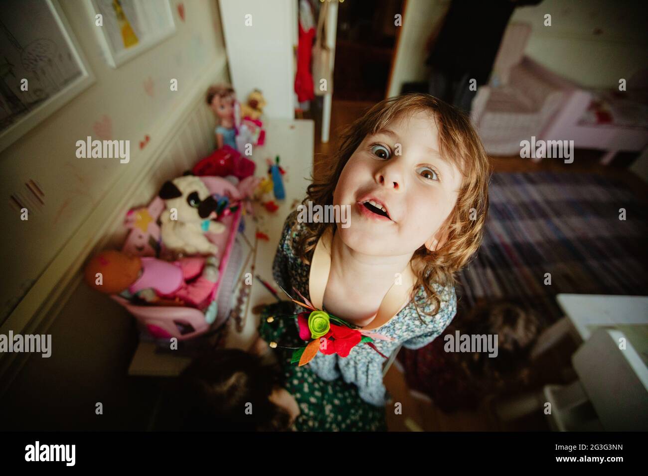 Dall'alto della bambina comica che guarda la macchina fotografica e fa i volti in sala giochi a casa Foto Stock