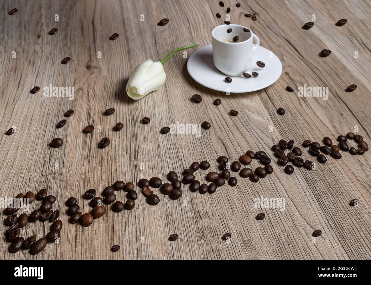 I chicchi di caffè formano la parola "buongiorno" con una tazza di caffè espresso su cui cadono altri chicchi Foto Stock