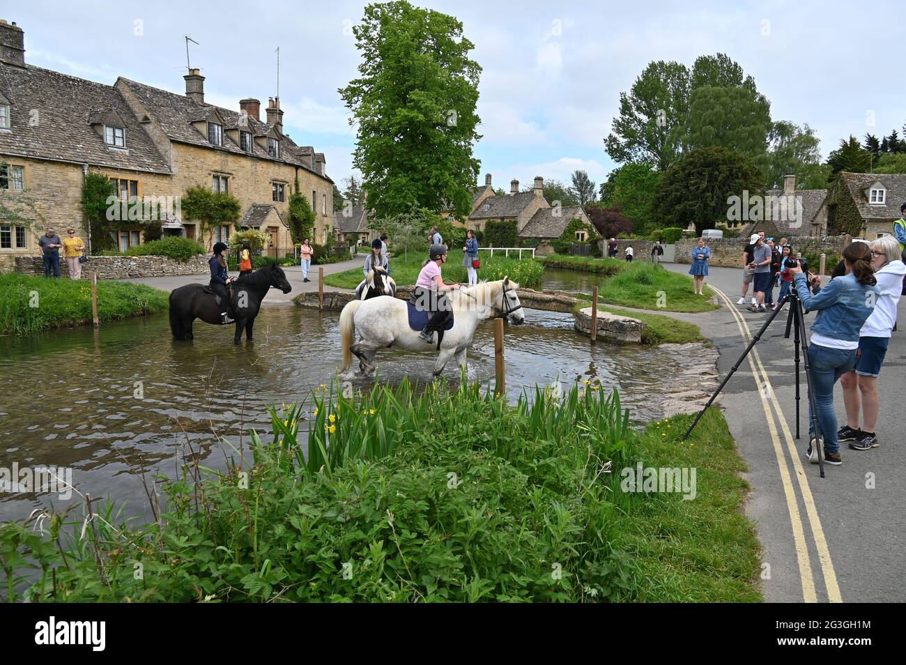 Cavalli su un hack nel River Eye nel villaggio di Cotswold di macellazione inferiore, mentre un fotografo e il suo studente li guardano emergere dal fiume. Foto Stock
