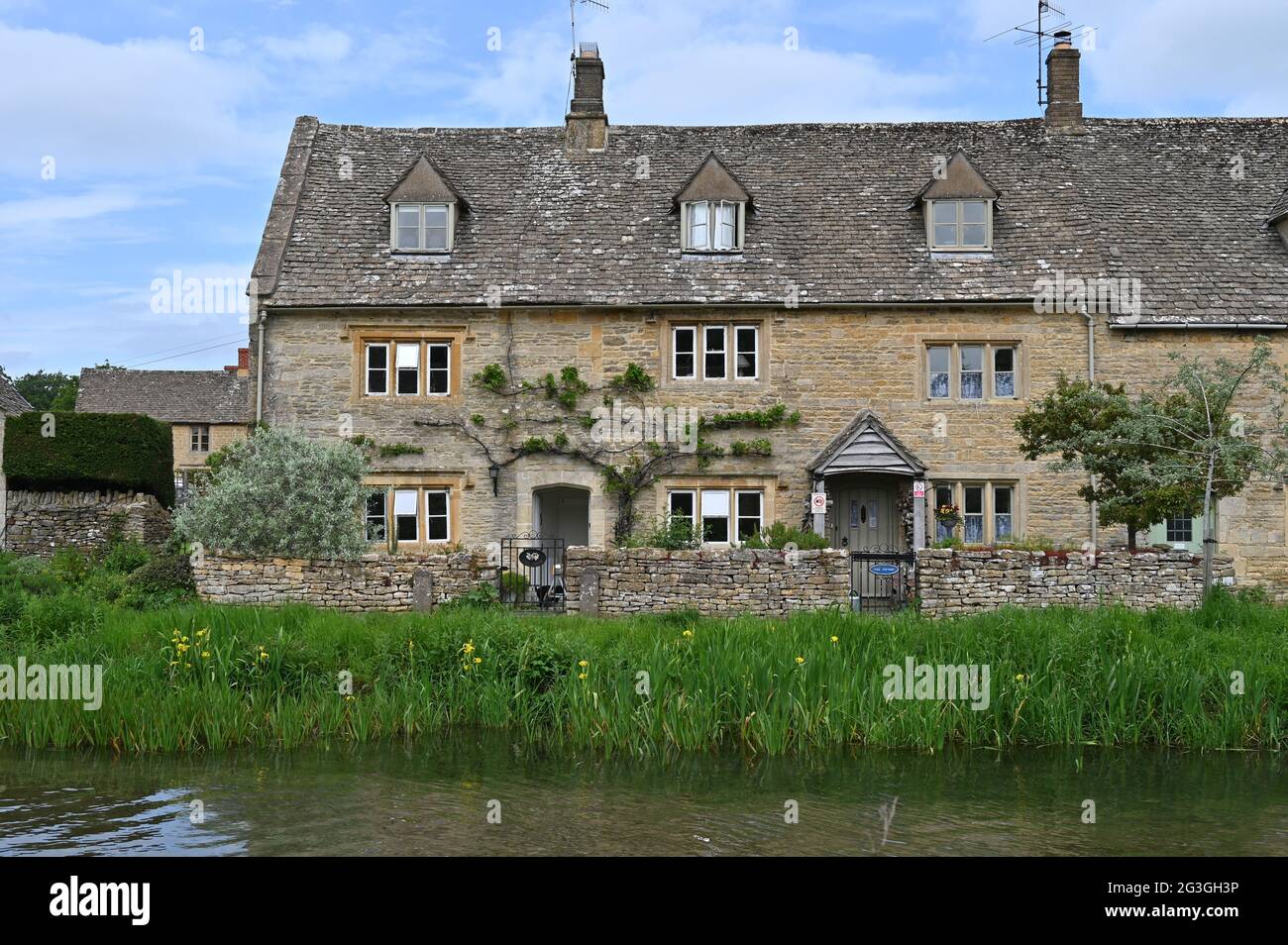 Una fila di case si trova vicino al River Eye che scorre attraverso il pittoresco villaggio di Lower Slaughter, una popolare destinazione turistica in questa parte o Foto Stock