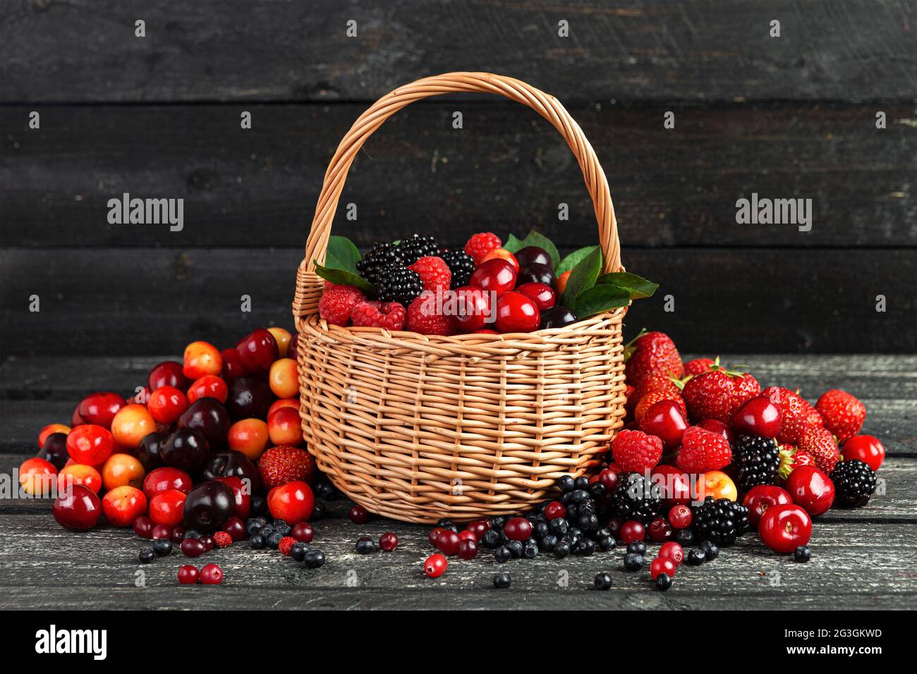 Frutti di bosco freschi in cesto di vimini su fondo di legno nero Foto Stock