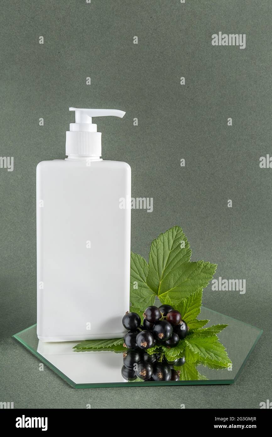 Flacone bianco cosmetico bianco con dispenser e punta di ribes nero su specchio, fondo verde. Naturale Organic Beauty concetto cosmetico. Vista frontale Foto Stock