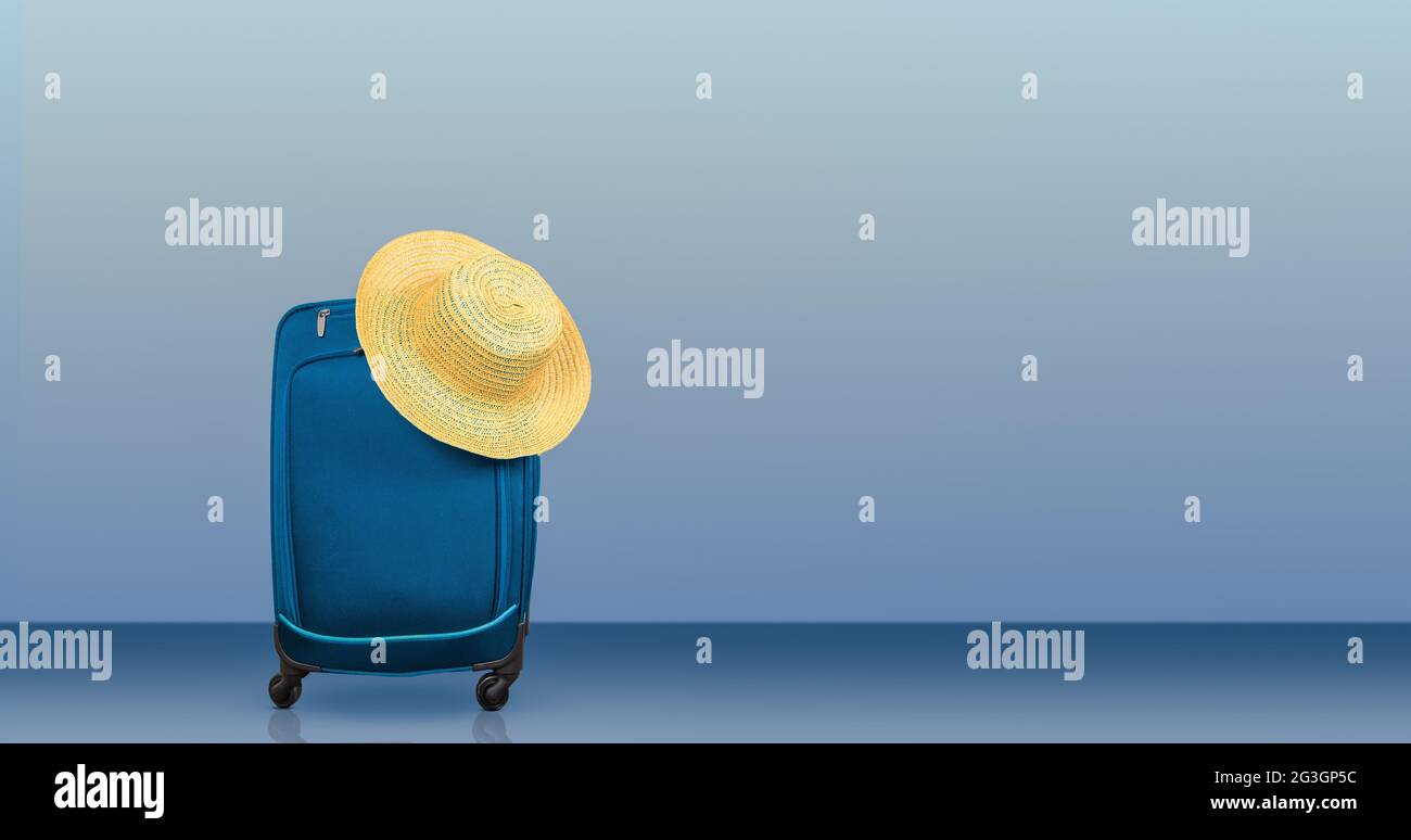 Valigia di viaggio e cappello estivo su sfondo blu. Concetto di viaggio e vacanza. Foto Stock