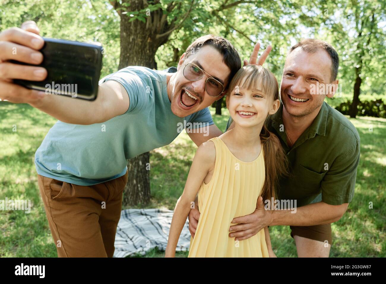 Coppia maschile gay che fa ritratto selfie sul telefono cellulare con figlia nel parco Foto Stock