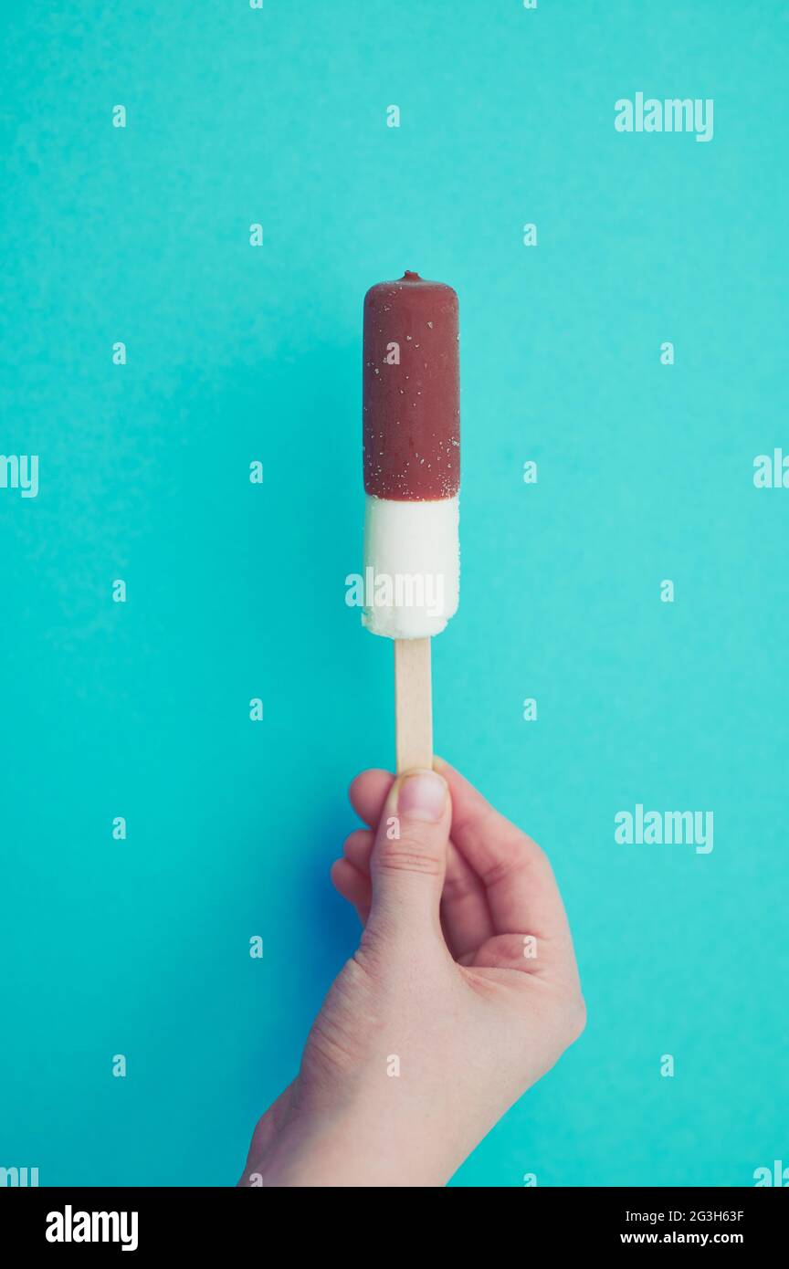 gelato alla vaniglia con cioccolato su un bastone tenuto dalla mano di un bambino, con spazio di copia su sfondo verde menta Foto Stock