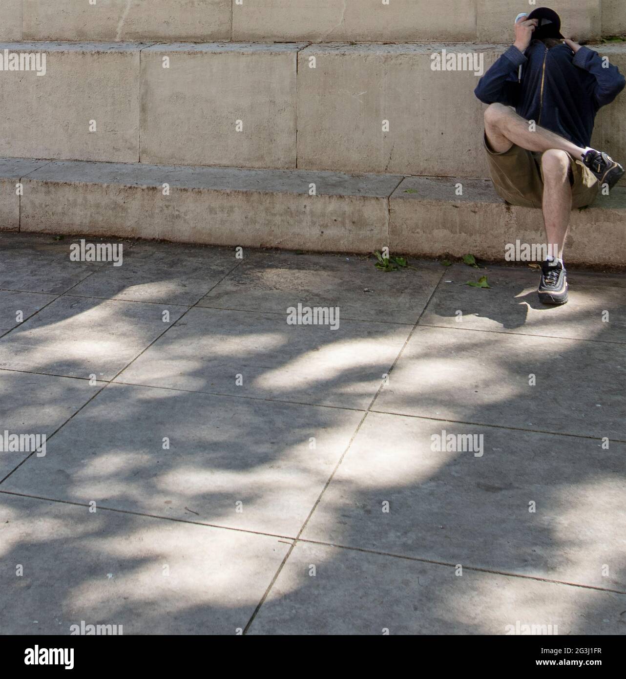 Uomo che cerca di nascondersi seduto sotto la luce del sole nel centro di Londra Foto Stock