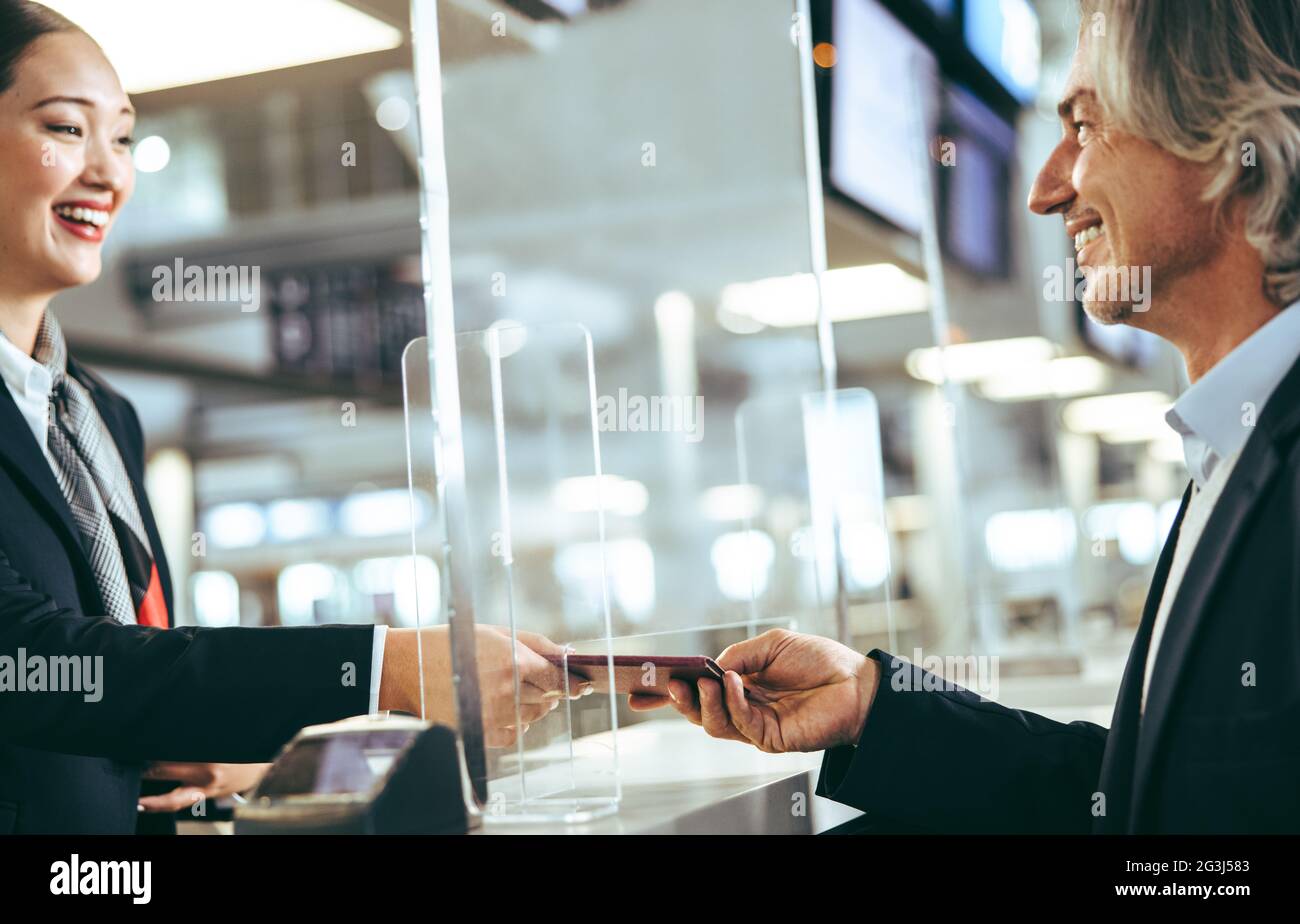 Uomo d'affari che effettua il check-in al terminal dell'aeroporto, consegnando il passaporto e il biglietto all'addetto di terra. Divisorio in vetro acrilico trasparente su t Foto Stock