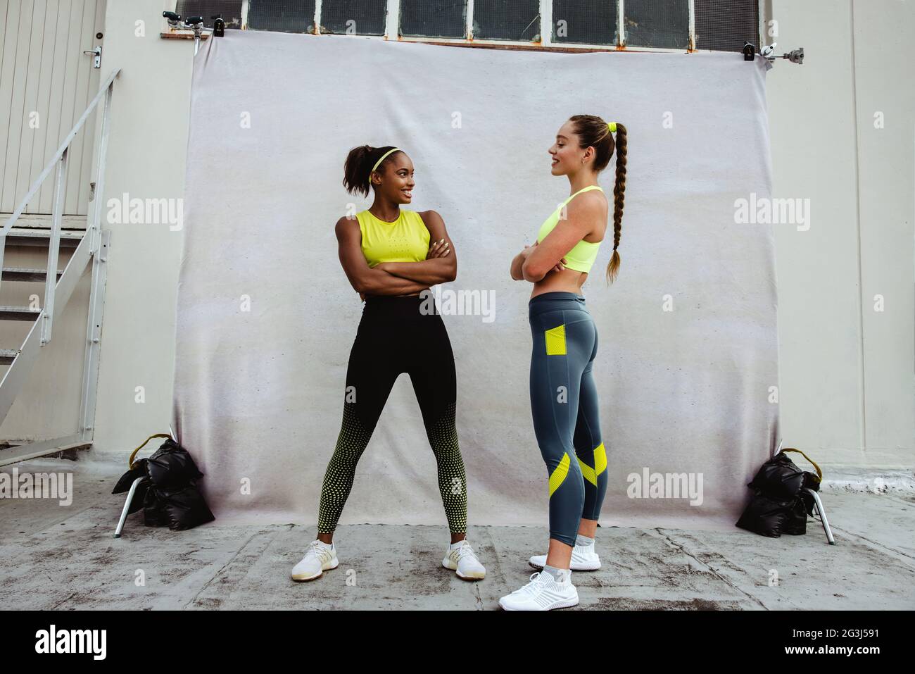Due donne in abbigliamento sportivo che si guardano l'una all'altra sul tetto. Donne sportive con braccia incrociate in piedi insieme e sorridenti. Foto Stock