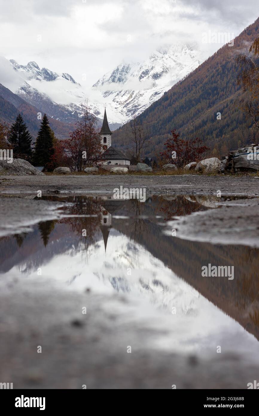 Moody svizzera chiesa in regione alpina riflesso in piccolo puddle Foto Stock