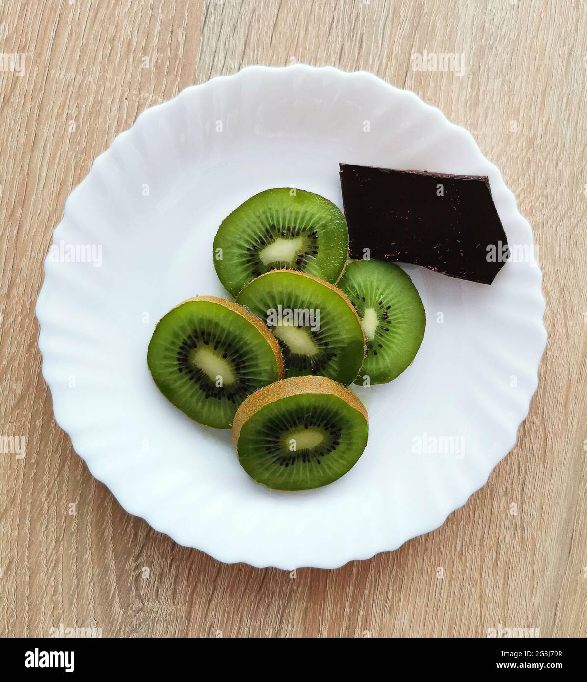 Alcuni pezzi di kiwi e un pezzo di cioccolato fondente su un piatto bianco Foto Stock