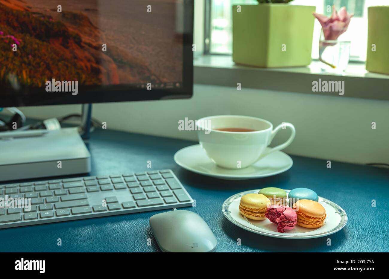 Piatto di macaron colorati e una tazza di tè dal computer. Foto Stock