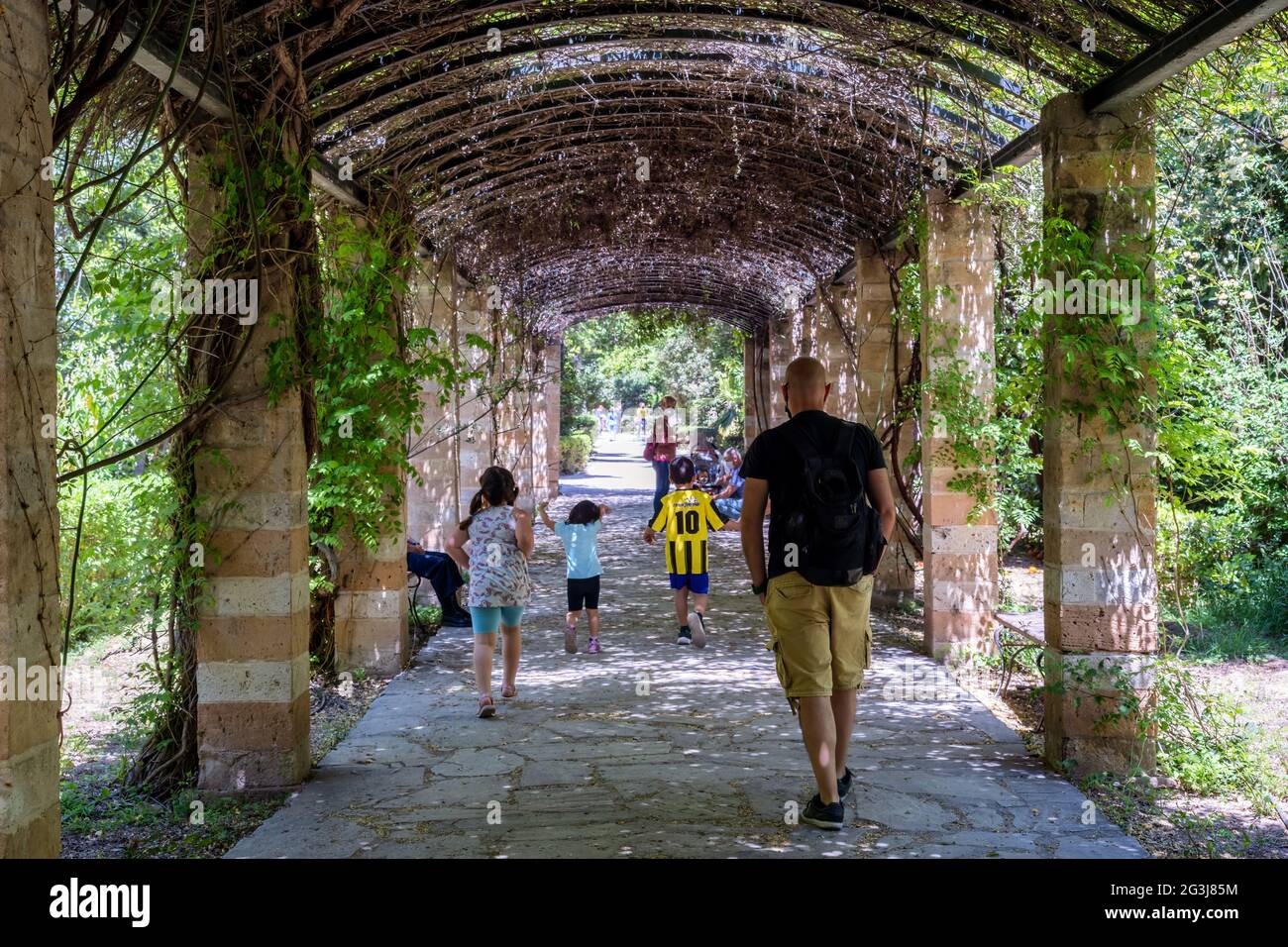 La Pergola di Amalia nel Giardino Nazionale di Atene. Persone che camminano, riposano o si rilassano sotto l'ombra del pergolato in una giornata di sole Foto Stock