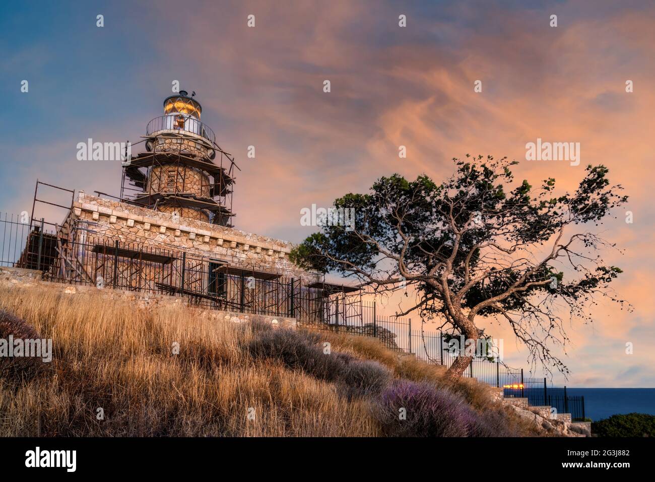 Isola di Salamis, Grecia. Il faro costruito in pietra a capo Koghi nell'isola di Salamis al tramonto con il cielo nuvoloso colorato Foto Stock