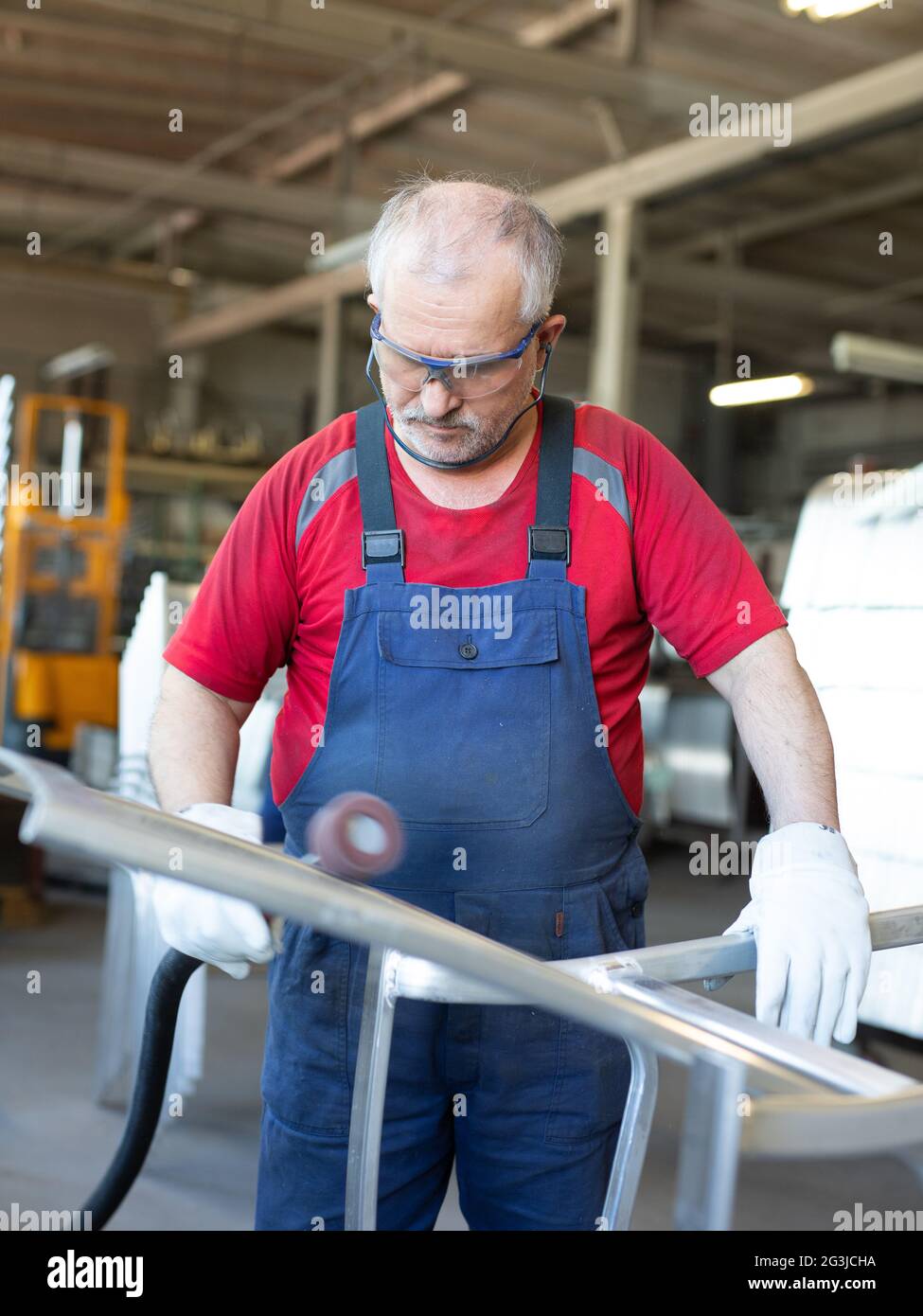 Il collarino blu che lucidano un pezzo di metallo in un impianto di produzione. Lucidatrice impegnata e concentrata mentre si lavora in una fabbrica. Foto Stock