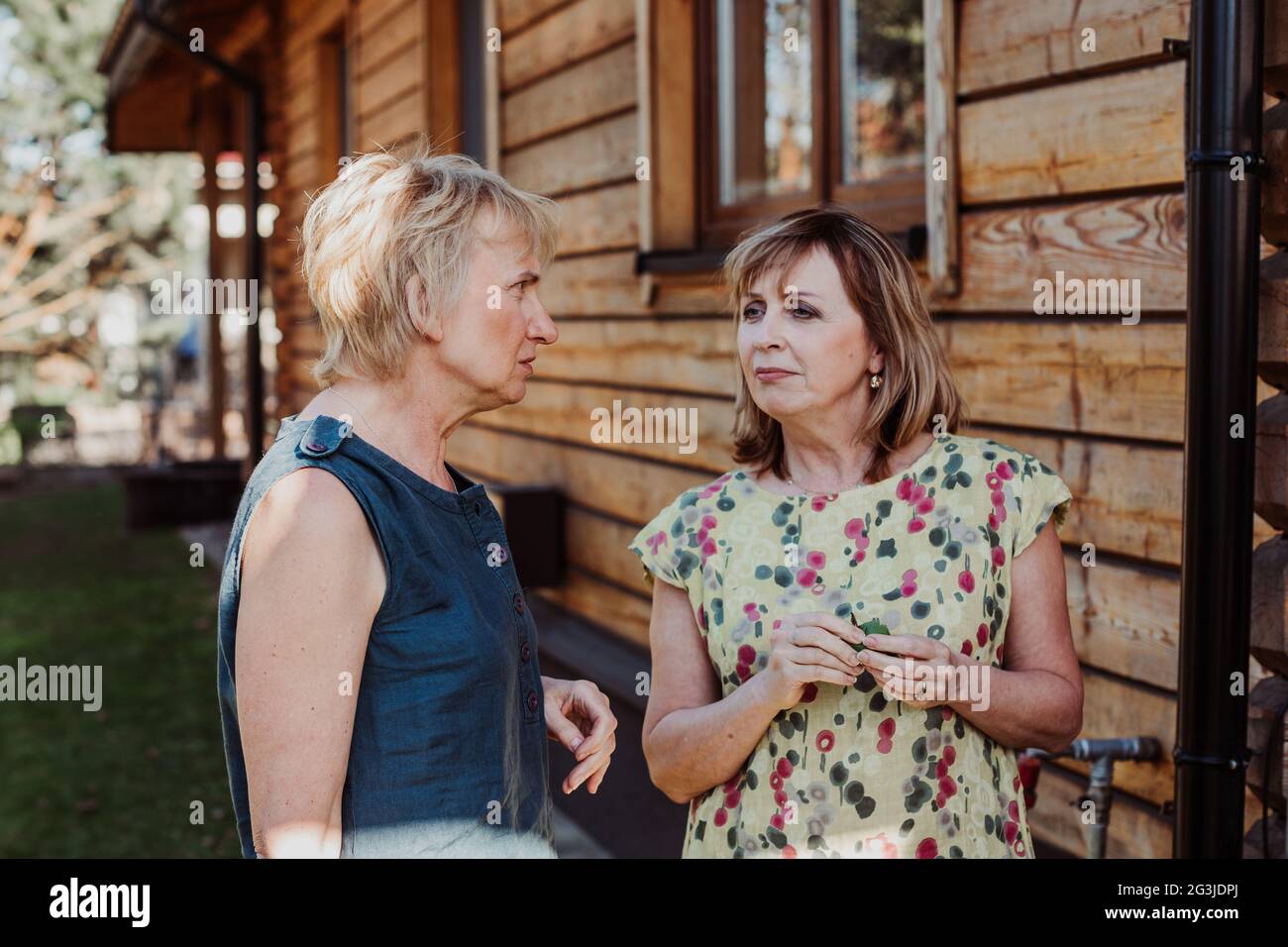 Due donne mature di 55 anni stanno parlando carino sullo sfondo di casa di legno Foto Stock