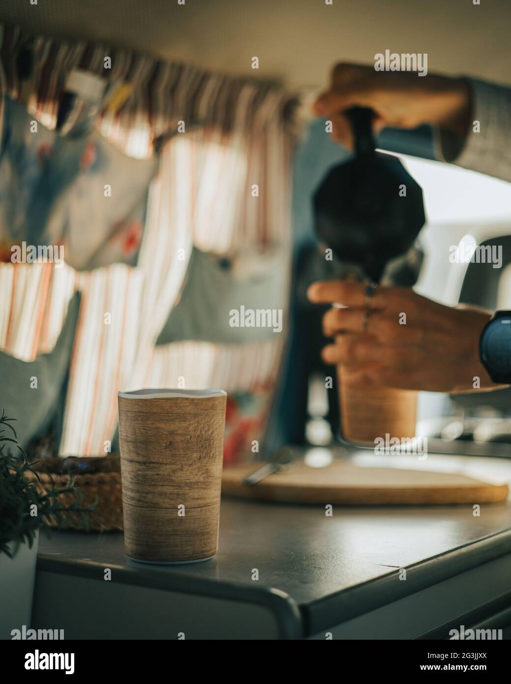 La persona del mattino presto serve caffè sullo sfondo da una caffettiera italiana a una tazza in un furgone in tonalità di caffè vintage mentre un'altra tazza aspetta Foto Stock