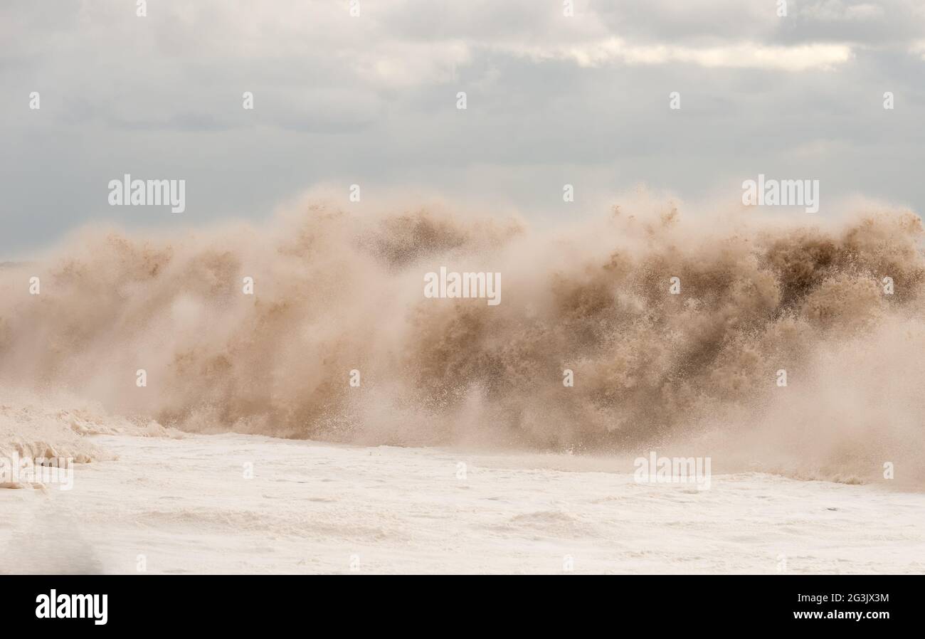 Onde giganti che si infrangono su una spiaggia. L'acqua sembra essere fangosa. Un sacco di spray fine (non è rumore). Schiuma di mare sulla sinistra. Cielo sovrastato. Un sacco di dettagli. Foto Stock