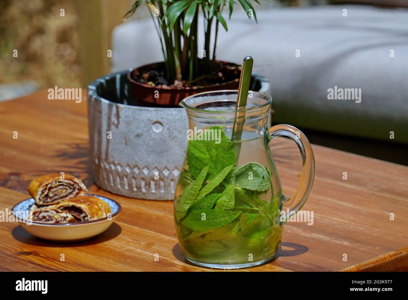 Caraffa di vetro di tè verde con foglie di menta su tavolo di legno con rotoli di noci e piante in vaso Foto Stock