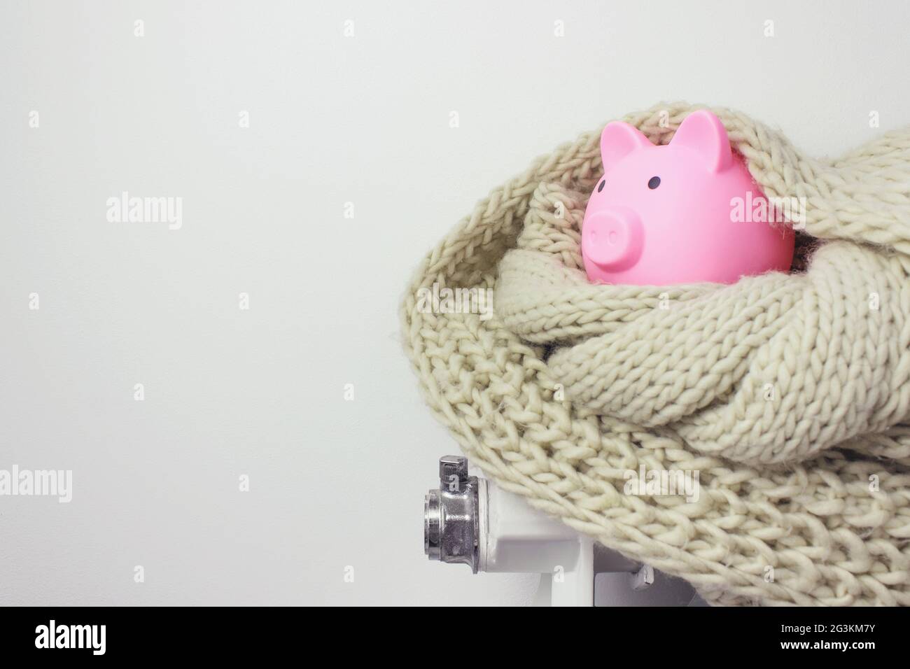 Banca di piggy con soldi e sciarpa sul radiatore. Concetto di stagione di riscaldamento. Foto Stock