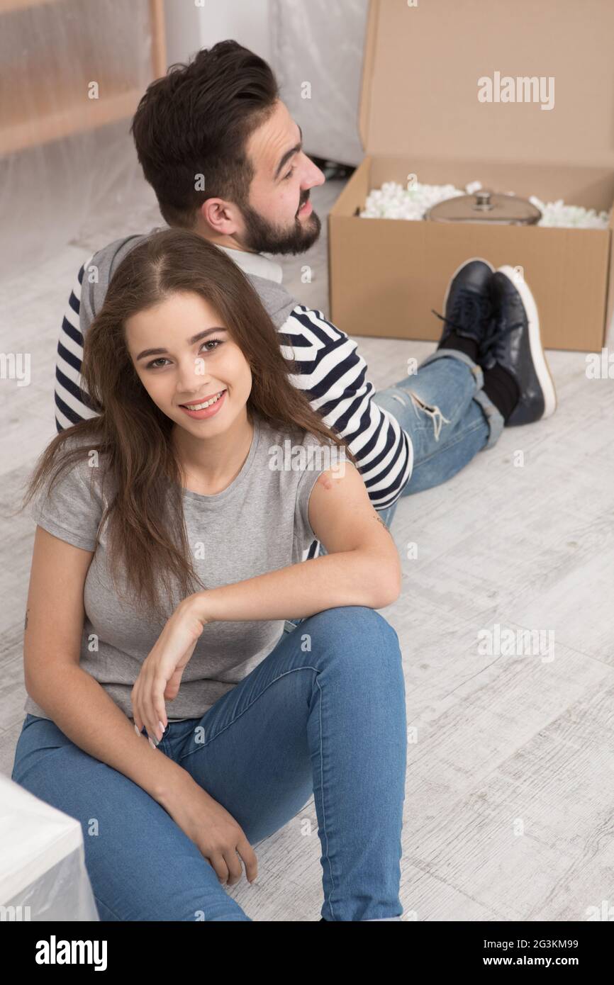 Felice l'uomo e la donna seduta sul pavimento stanco la preparazione di trasferirsi in un nuovo appartamento. Foto Stock