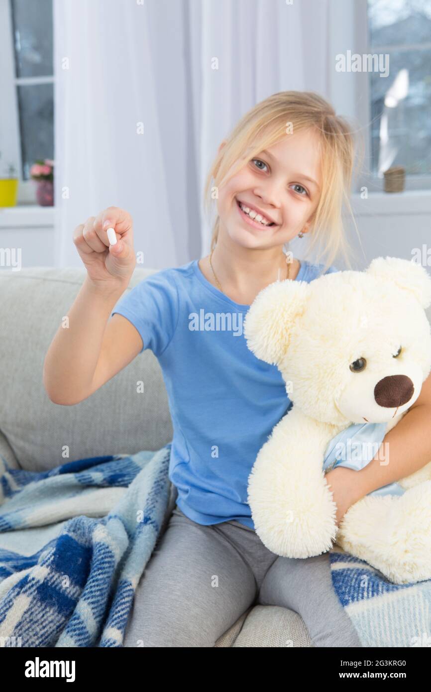 Bambina malata con viso pallido sorridente seduta sul divano. Foto Stock