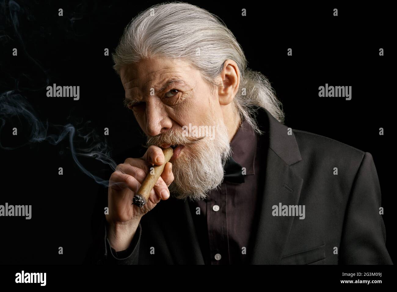 Uomo elegante invecchiato con sigaro lungo grigio fumo capelli. Foto Stock