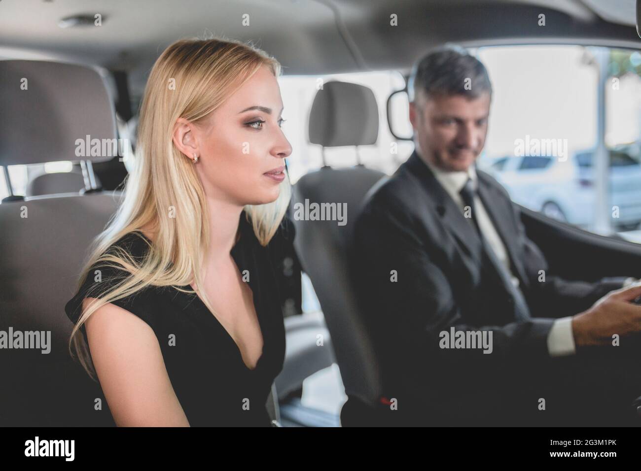 Concessionario che mostra auto elettrica a giovane donna in salone auto. Foto Stock