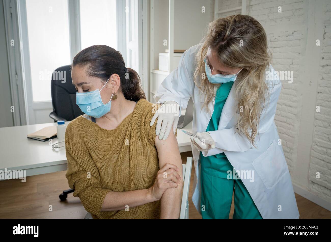 Medico femminile o infermiera che vaccina la giovane donna in clinica. Paziente di sesso maschile vaccinato contro Coronavirus che riceve vaccino covid per via intramuscolare in Foto Stock