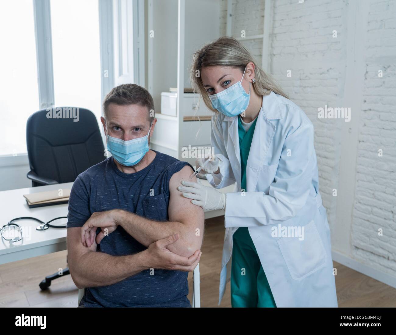 Medico femminile o infermiera che vaccina il giovane in clinica. Paziente di sesso maschile vaccinato contro Coronavirus che riceve vaccino covid per via intramuscolare Inje Foto Stock