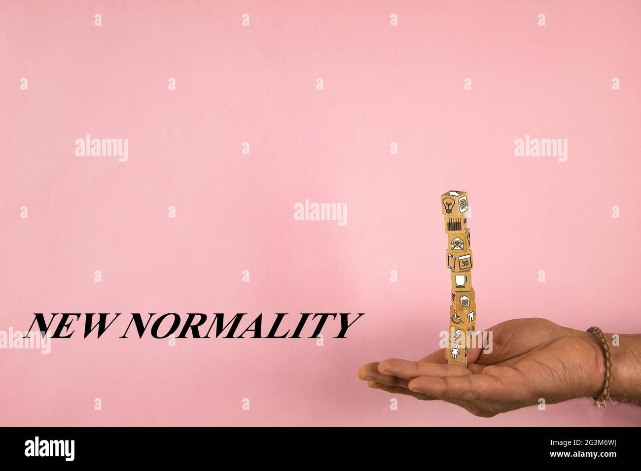 mano che tiene una pila di blocchi di legno in equilibrio con le forme e il concetto di nuova normalità su uno sfondo rosa Foto Stock