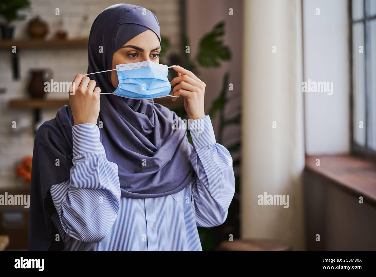 Donna musulmana che mette una maschera medica sul viso Foto Stock