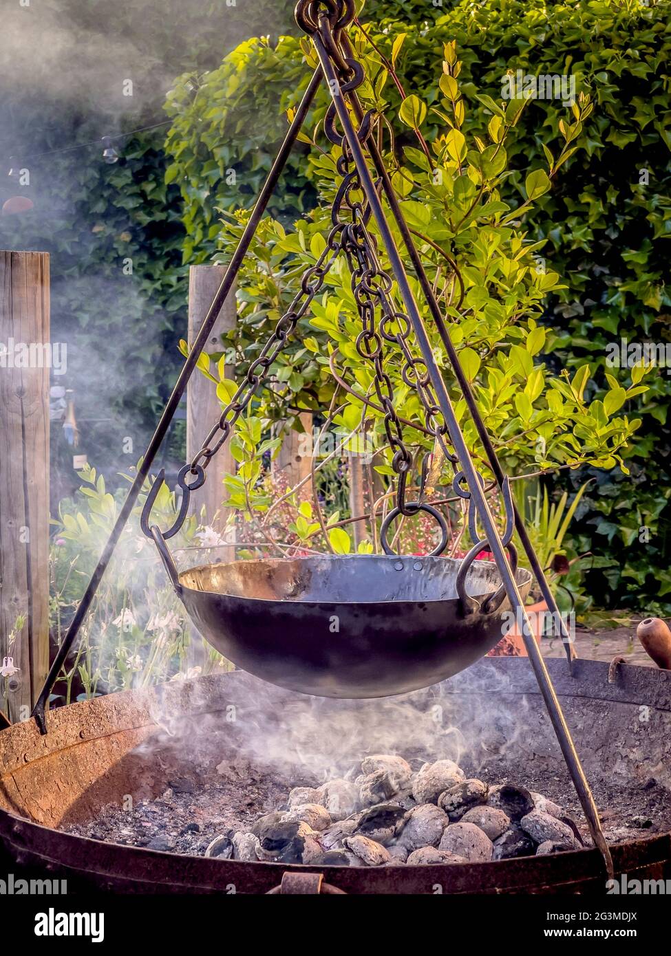 Cucina all'aperto con carbone in ciotola fuoco con treppiede e pentola appesa alle catene Foto Stock