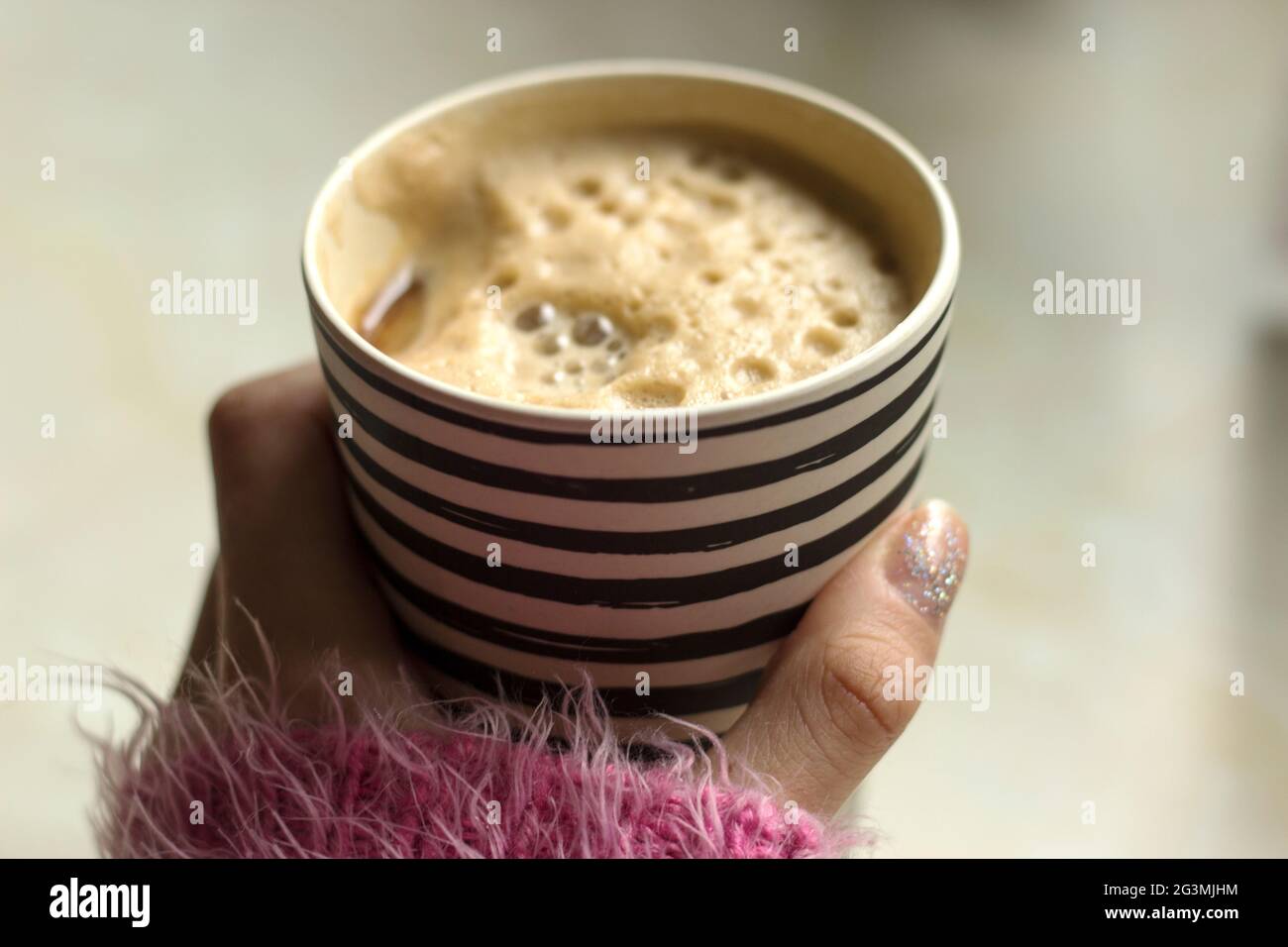 La donna sta tenendo una tazza di viaggio di bambù con caffè schiumoso e latte di soia/soia. Tazza di caffè Stripey sul banco Foto Stock