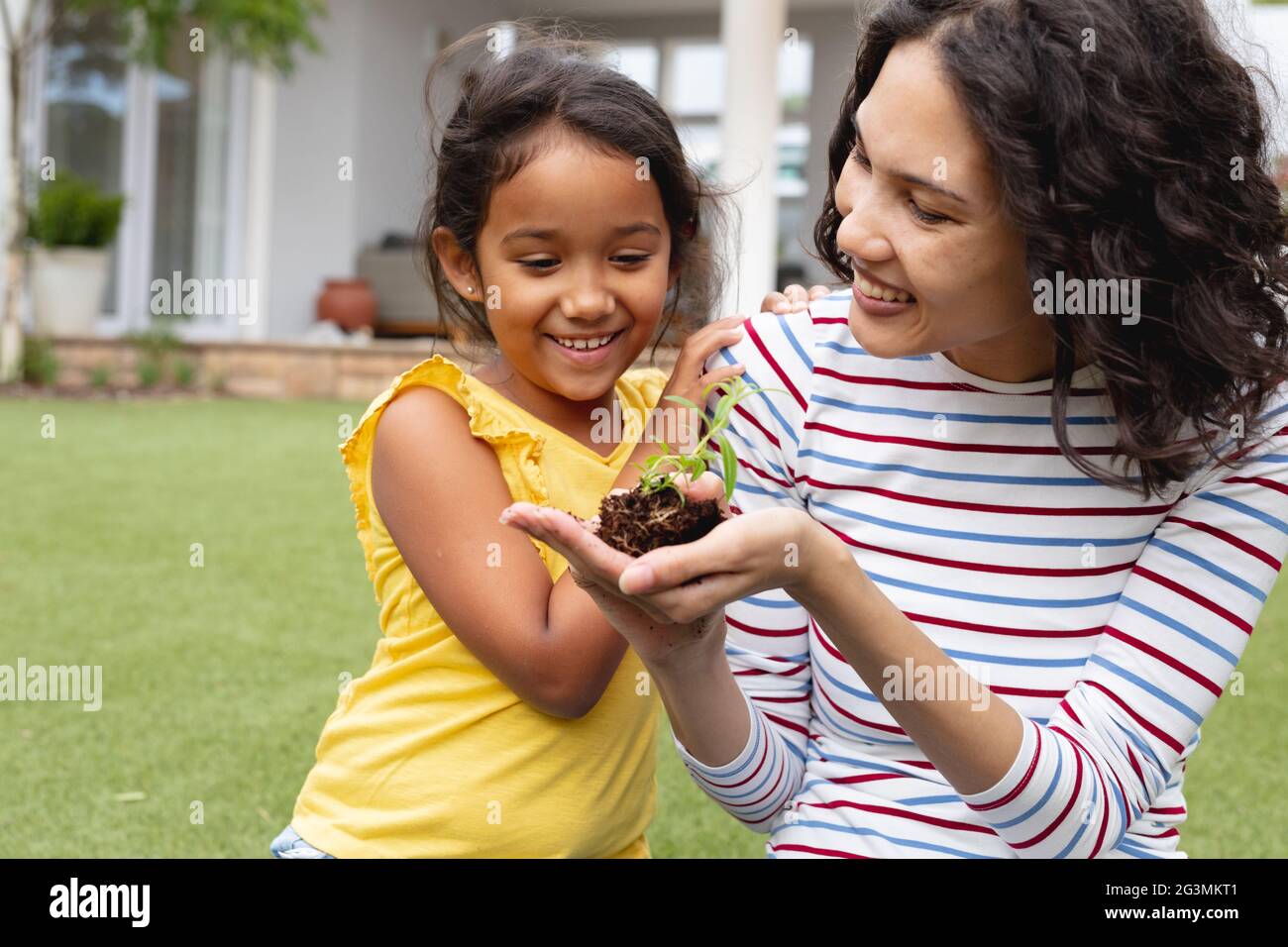 Sorridente giardinaggio di madre e figlia ispanica, madre che tiene il seedling in mano Foto Stock