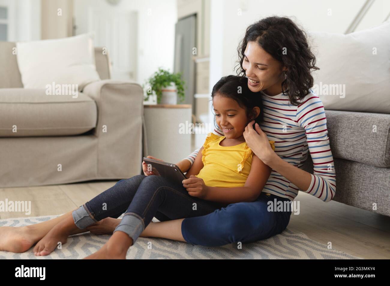 Sorridi madre e figlia ispanica seduti sul pavimento del soggiorno usando insieme un tablet Foto Stock