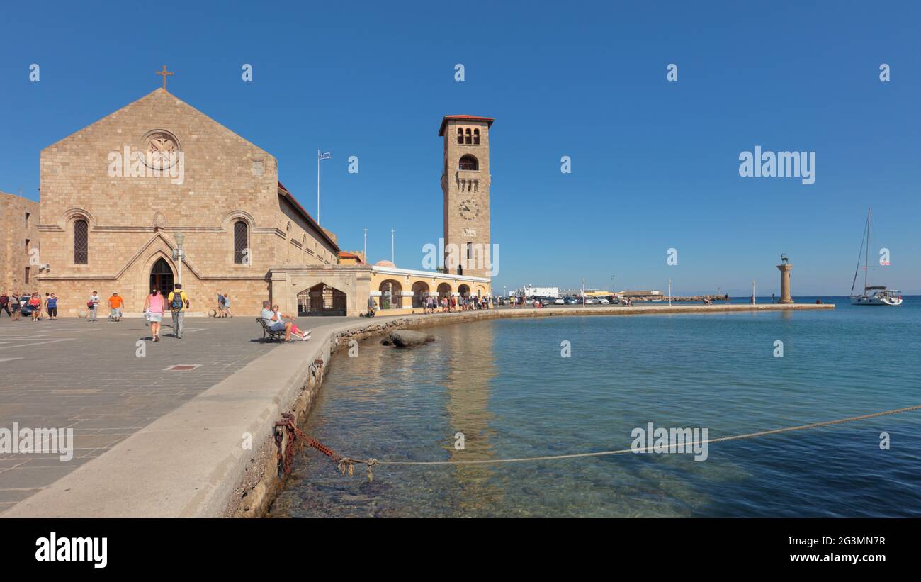 Persone che riposano al porto di Mandraki di Rodi, isola di Rodi, Grecia contro la Chiesa di Annunciazione della Vergine nella città di Rodi, Dodecanese Foto Stock