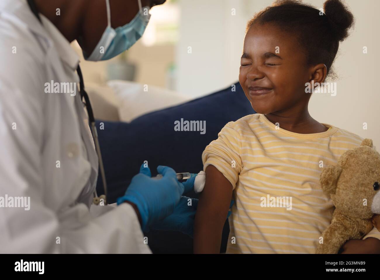 African american femmina medico in maschera di faccia che dà la vaccinazione di covid a paziente di ragazza spaventata a casa Foto Stock