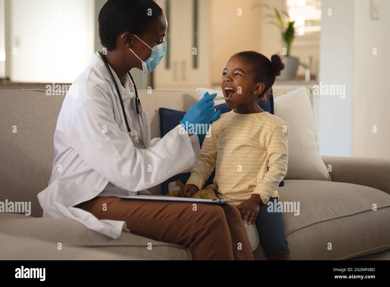 African american femmina medico in maschera facciale che dà la ragazza paziente covid test tampone a casa Foto Stock