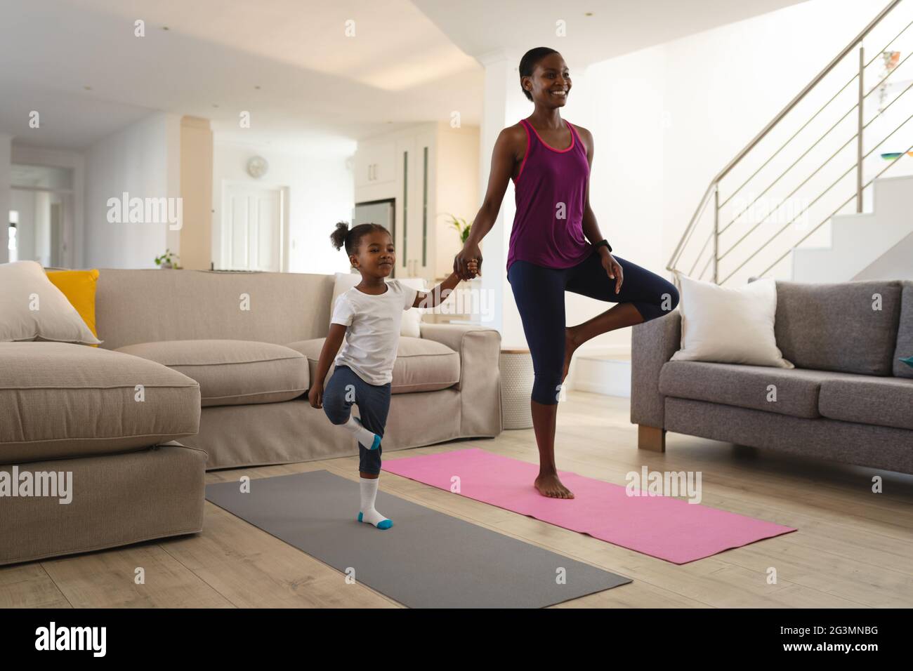 Sorridente madre afroamericana e figlia che pratica yoga tenendo le mani e in piedi su una gamba Foto Stock