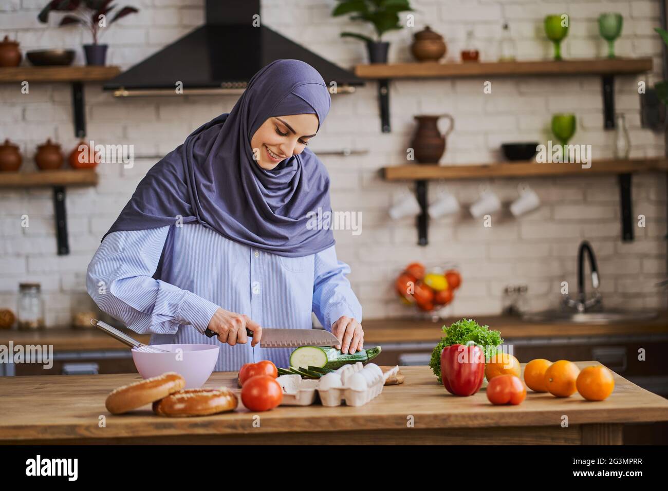 Giovane donna araba che taglia una zucchina e sorride Foto Stock