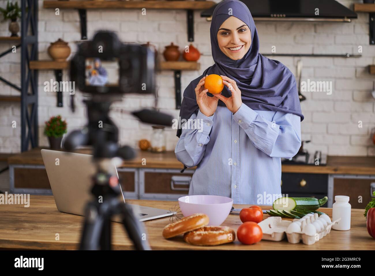 Splendida donna musulmana che tiene un arancione e parla con la fotocamera con un sorriso Foto Stock