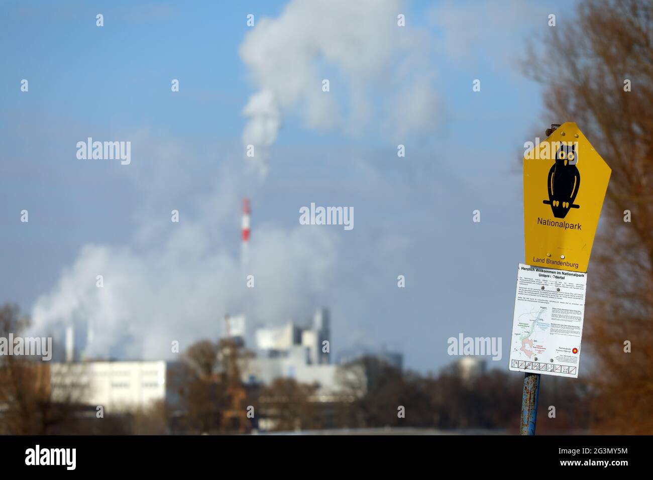 '10.02.2021, Schwedt, Brandeburgo, Germania - cartello del Parco Nazionale. Sullo sfondo, i gas di scarico fuoriescono dai camini del Leipa Georg Leinfelder G. Foto Stock