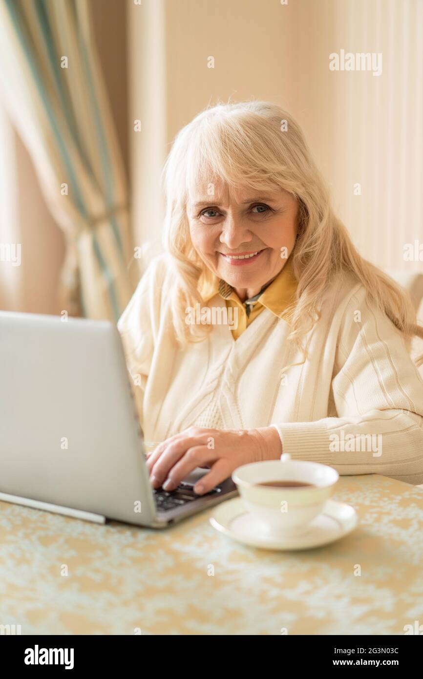 Donna anziana al computer portatile che si rilassa a casa seduto al tavolo Foto Stock