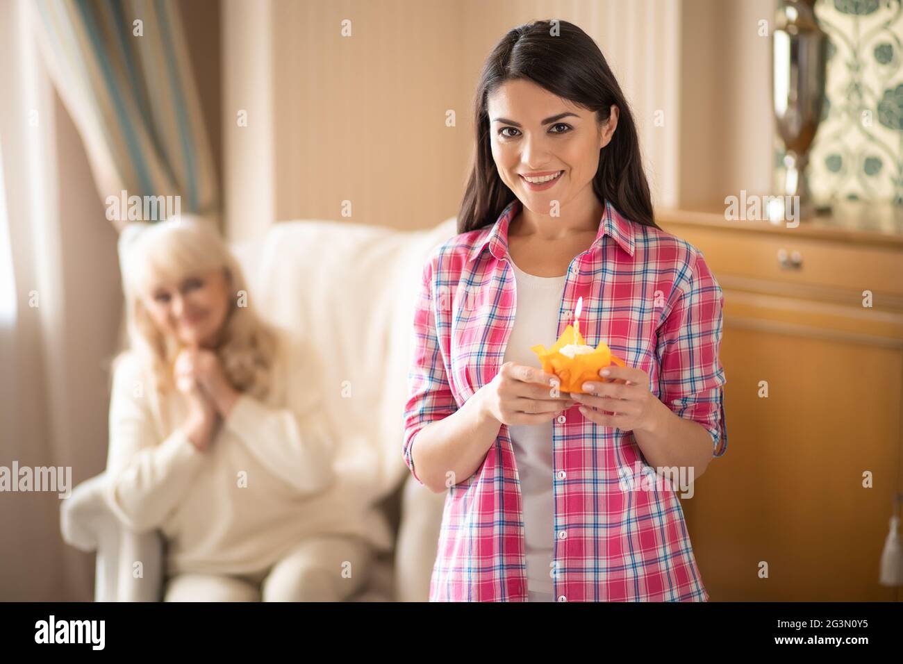 La figlia affascinante dà la piccola cupcake di compleanno con la candela alla sua madre più anziana Foto Stock