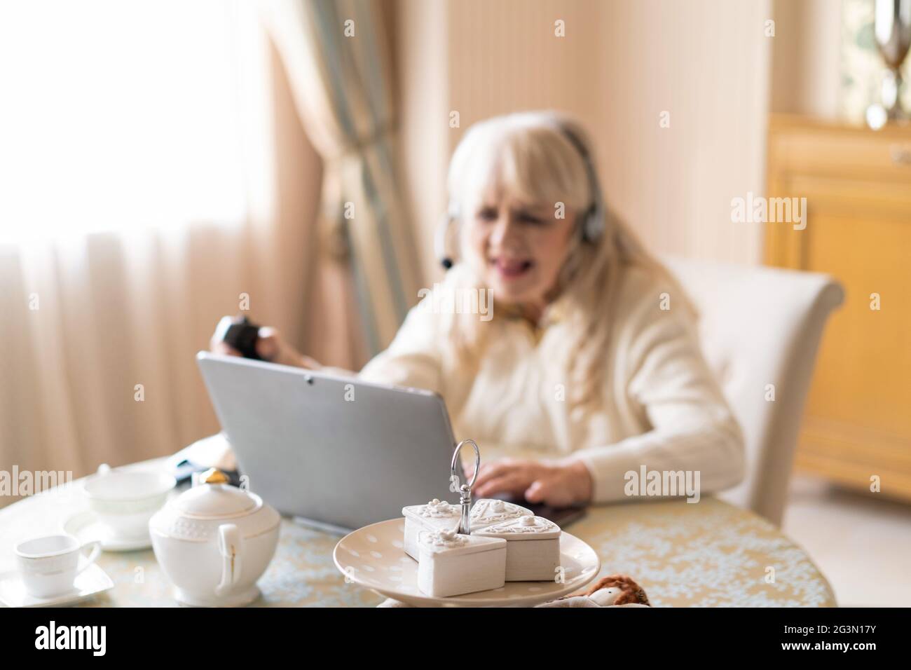 La donna anziana gioca ai videogiochi con il joystick su un laptop Foto Stock