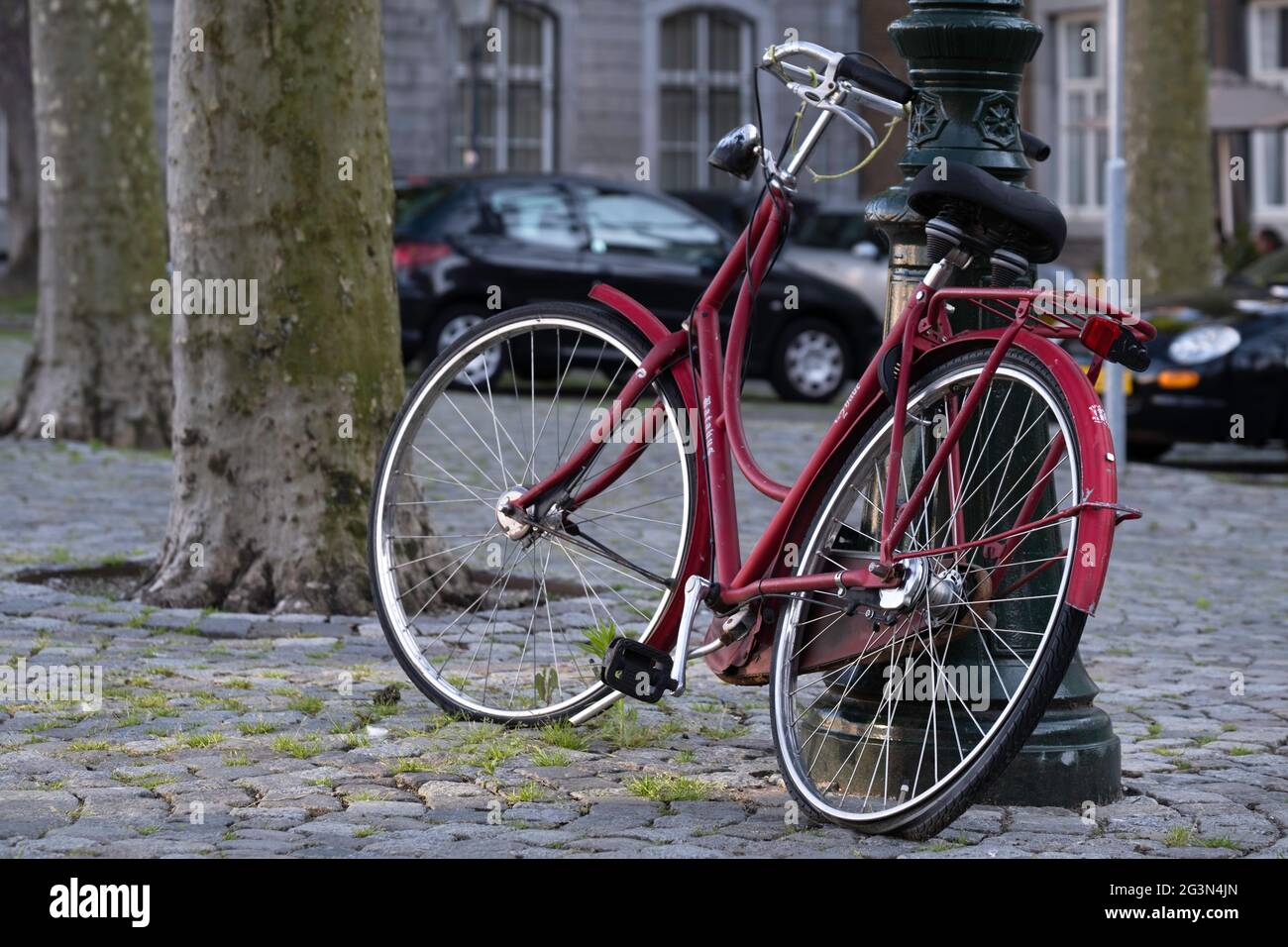 La bicicletta rossa con pneumatico posteriore piatto è bloccata contro un lampione antico su una piazza a Maastricht Foto Stock