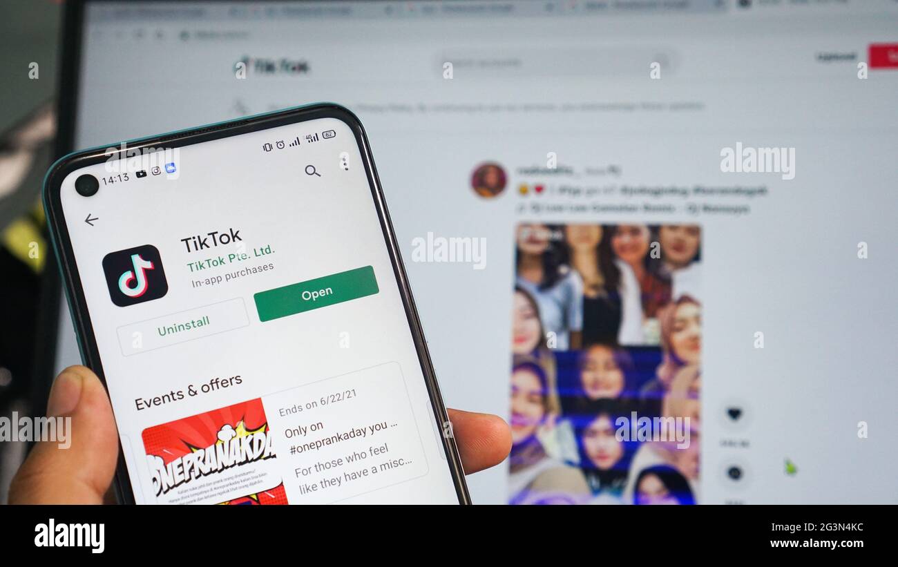Dumai, indonesia - Giugno 17,2021: La mano dell'uomo asiatico sta tenendo un telefono cellulare e sta aprendo l'app TIKTOK, con sfondo laptop Foto Stock