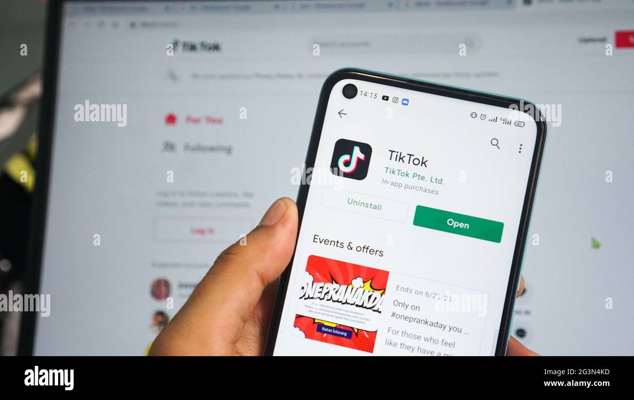 Dumai, indonesia - Giugno 17,2021: La mano dell'uomo asiatico sta tenendo un telefono cellulare e sta aprendo l'app TIKTOK, con sfondo laptop Foto Stock